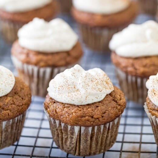 Pumpkin spice cupcakes with frosting on a baking rack.