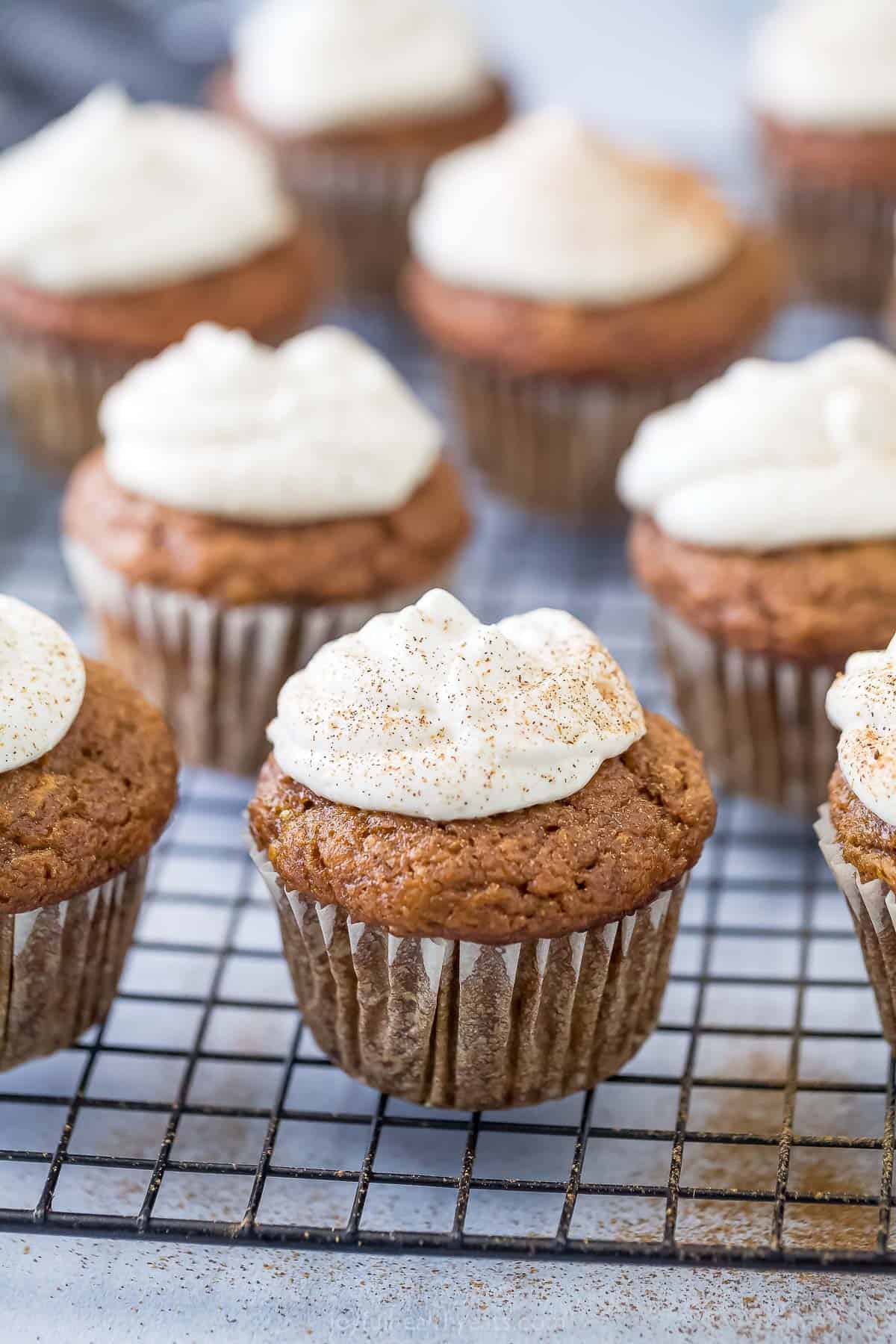 Pumpkin spice cupcakes with frosting on a baking rack. 