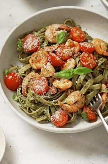 Angled photo of freshly made pesto pasta with sauteed shrimp, cherry tomatoes, and parmesan cheese.