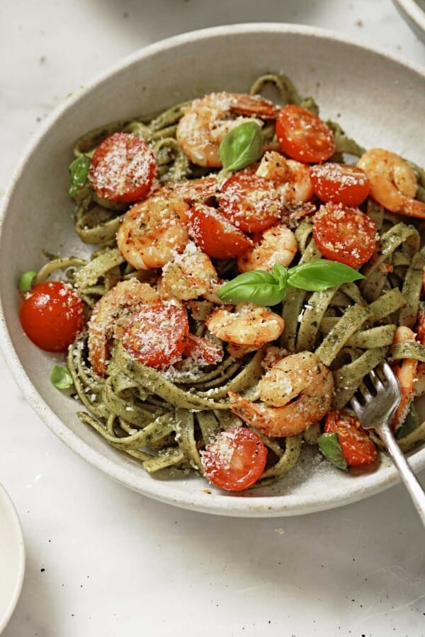 Angled photo of freshly made pesto pasta with sauteed shrimp, cherry tomatoes, and parmesan cheese.