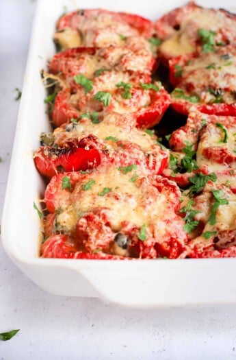 Bright red turkey stuffed pepper halves in a white baking dish with handles