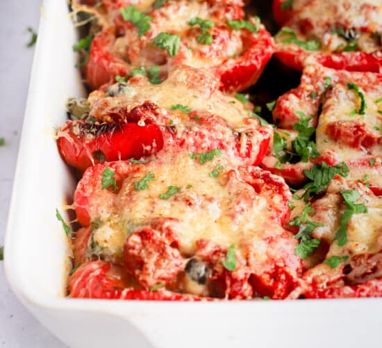 Bright red turkey stuffed pepper halves in a white baking dish with handles