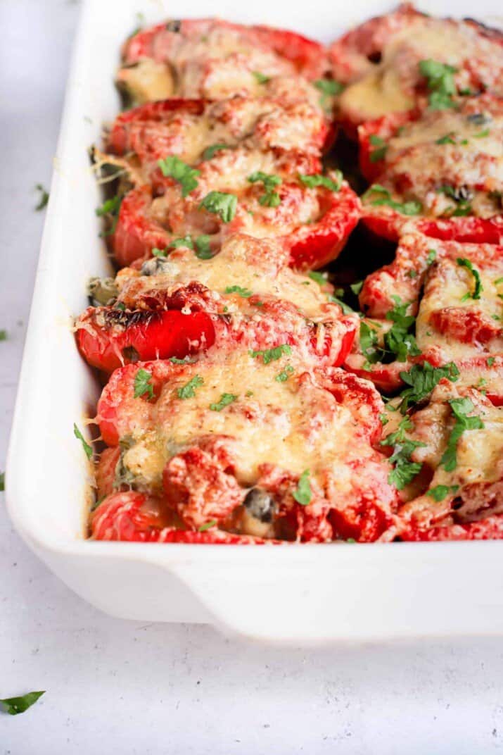 Bright red turkey stuffed pepper halves in a white baking dish with handles