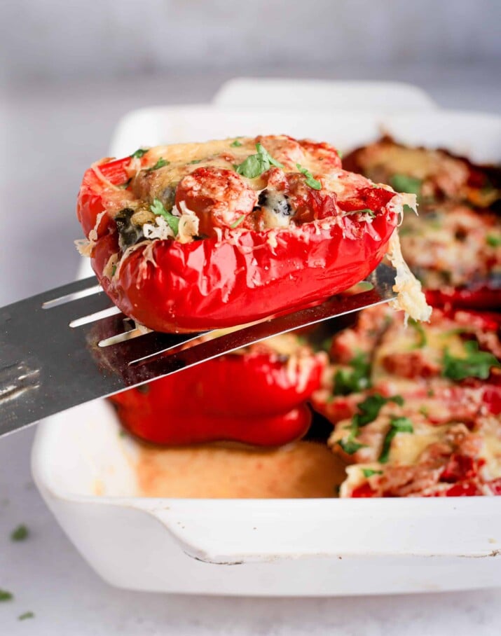 A spatula holding a single Southwestern turkey stuffed pepper half over a pan containing the remaining stuffed peppers