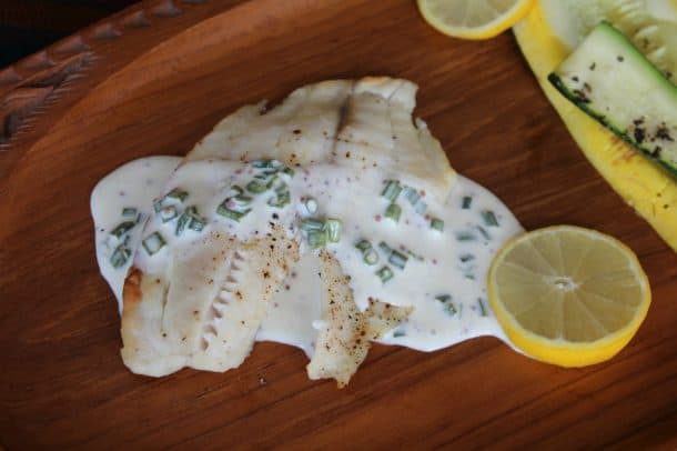 A fillet of broiled tilapia covered in Mustard Chive Sauce next to a slice of lemon.