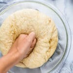 A hand punching down a ball of whole wheat pizza dough in a bowl