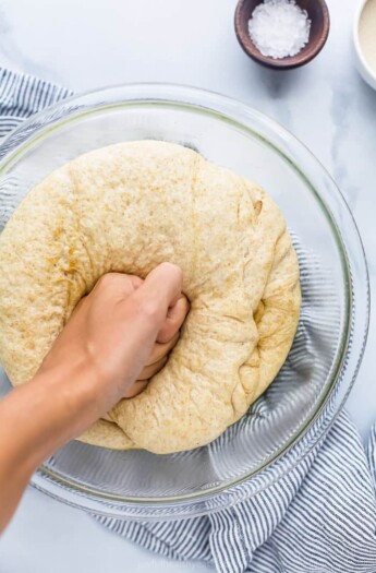 A hand punching down a ball of whole wheat pizza dough in a bowl