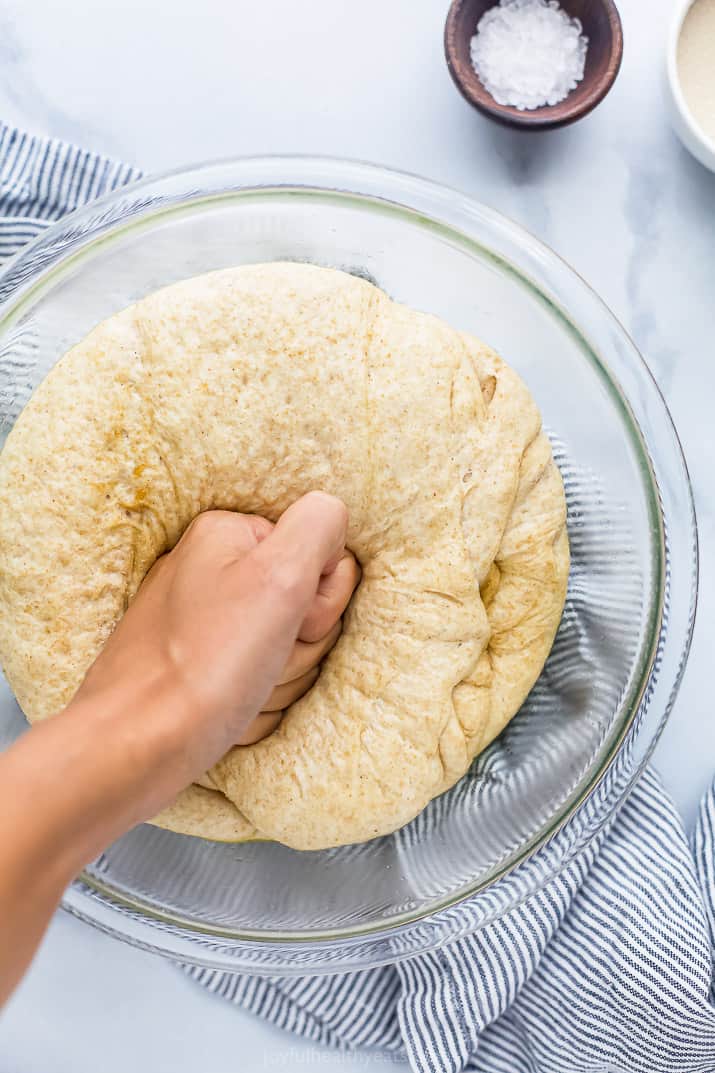 Top view of a hand punching down whole wheat pizza dough in a bowl