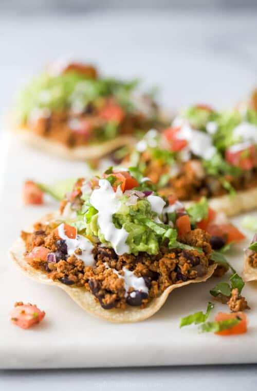 Assembled turkey tostadas recipe with sour cream, diced tomatoes, shredded lettuce, and guacamole on top.