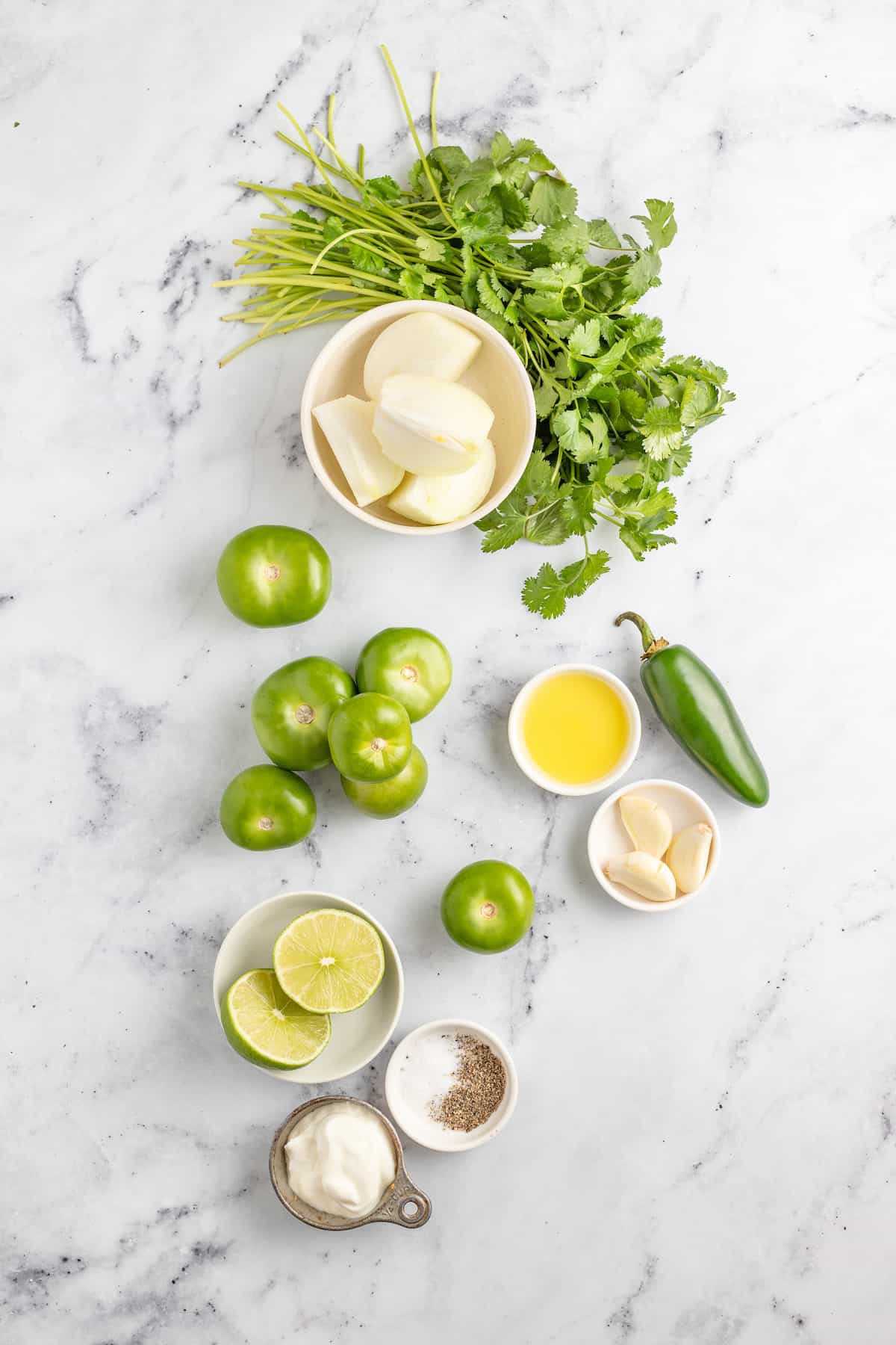Creamy Chicken Enchiladas Verdes are perfect for big family dinners. They're cheesy and creamy with just the right amount of heat! limes, cilantro, tomatillos, jalapeno, and other ingredient on a marble countertop