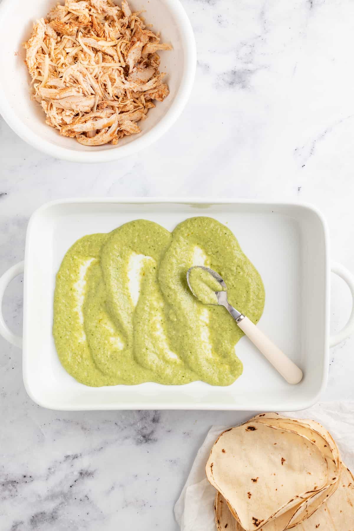 speading green sauce in a white casserole dish