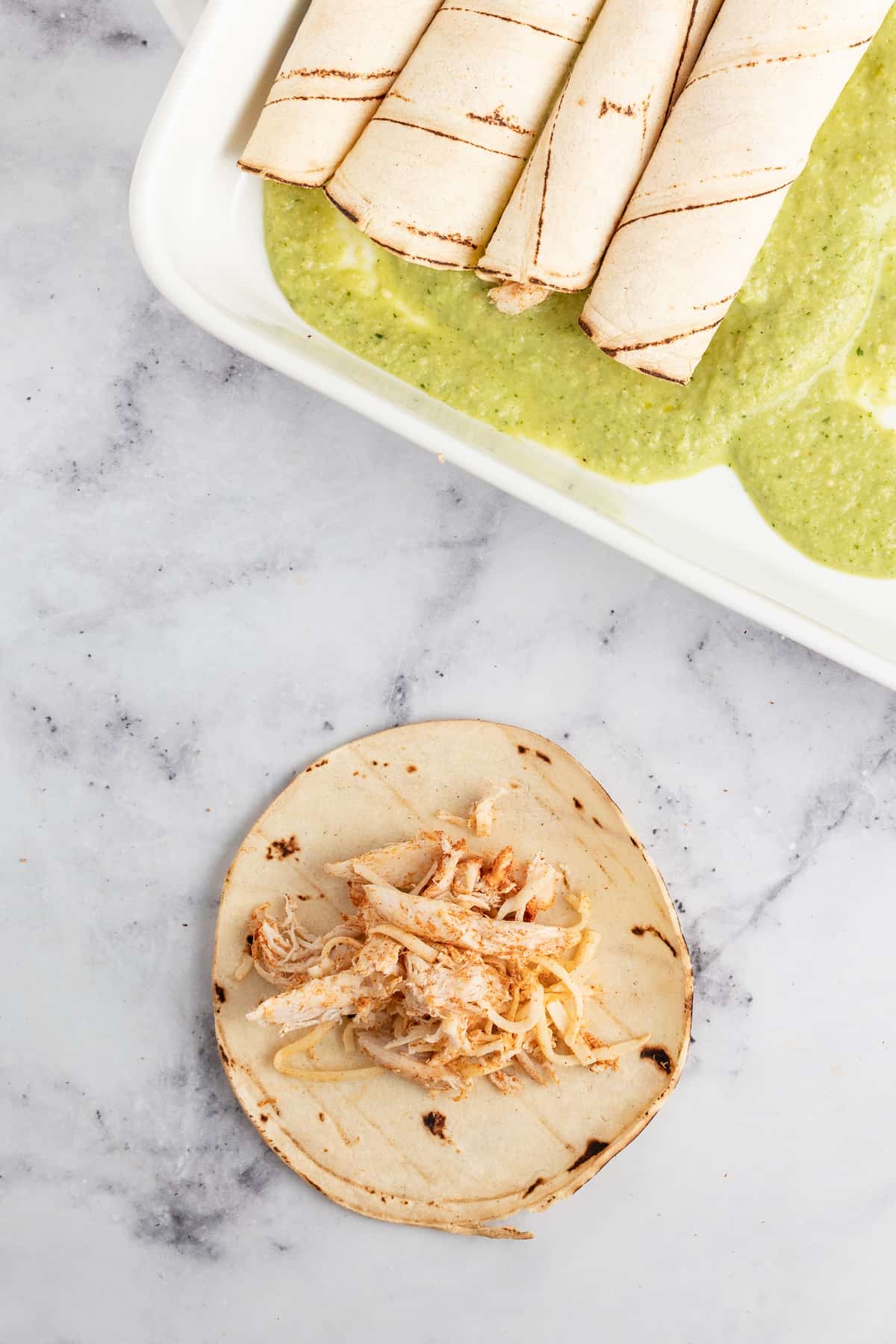 a plate with rolled tortillas and one tortilla with a scoop of chicken