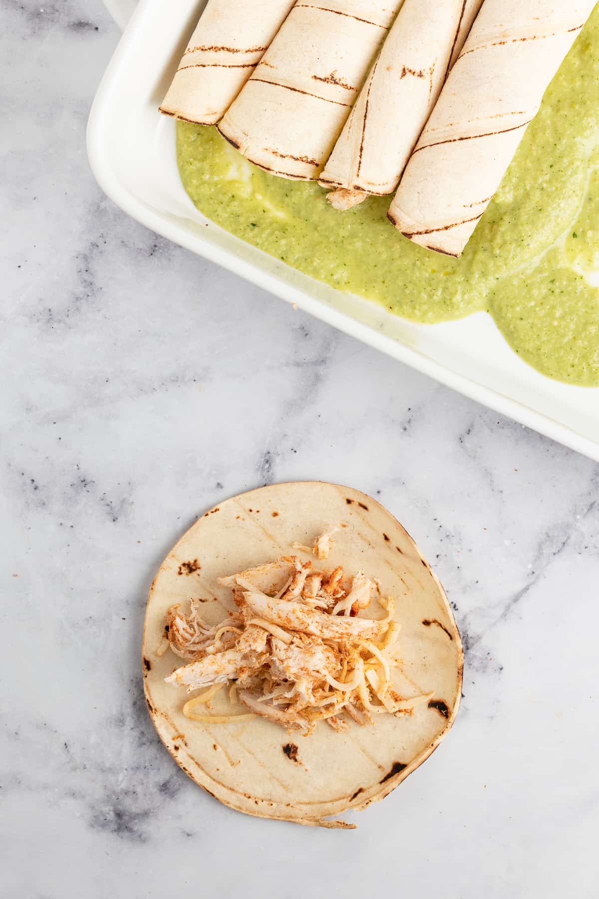 Creamy Chicken Enchiladas Verdes are perfect for big family dinners. They're cheesy and creamy with just the right amount of heat! a plate with rolled tortillas and one tortilla with a scoop of chicken