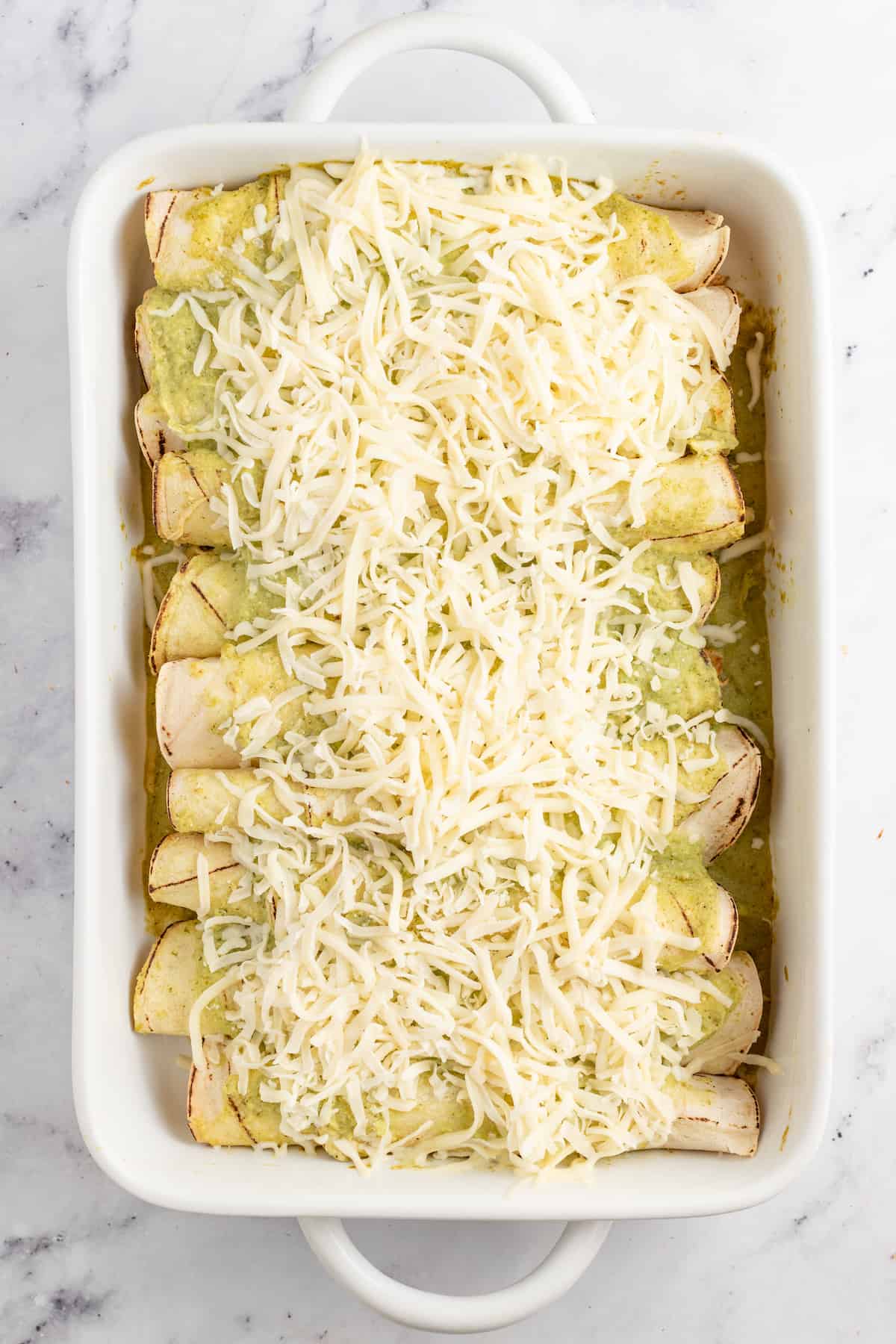 Creamy Chicken Enchiladas Verdes are perfect for big family dinners. They're cheesy and creamy with just the right amount of heat! casserole dish with chicken enchiladas and cheese on top