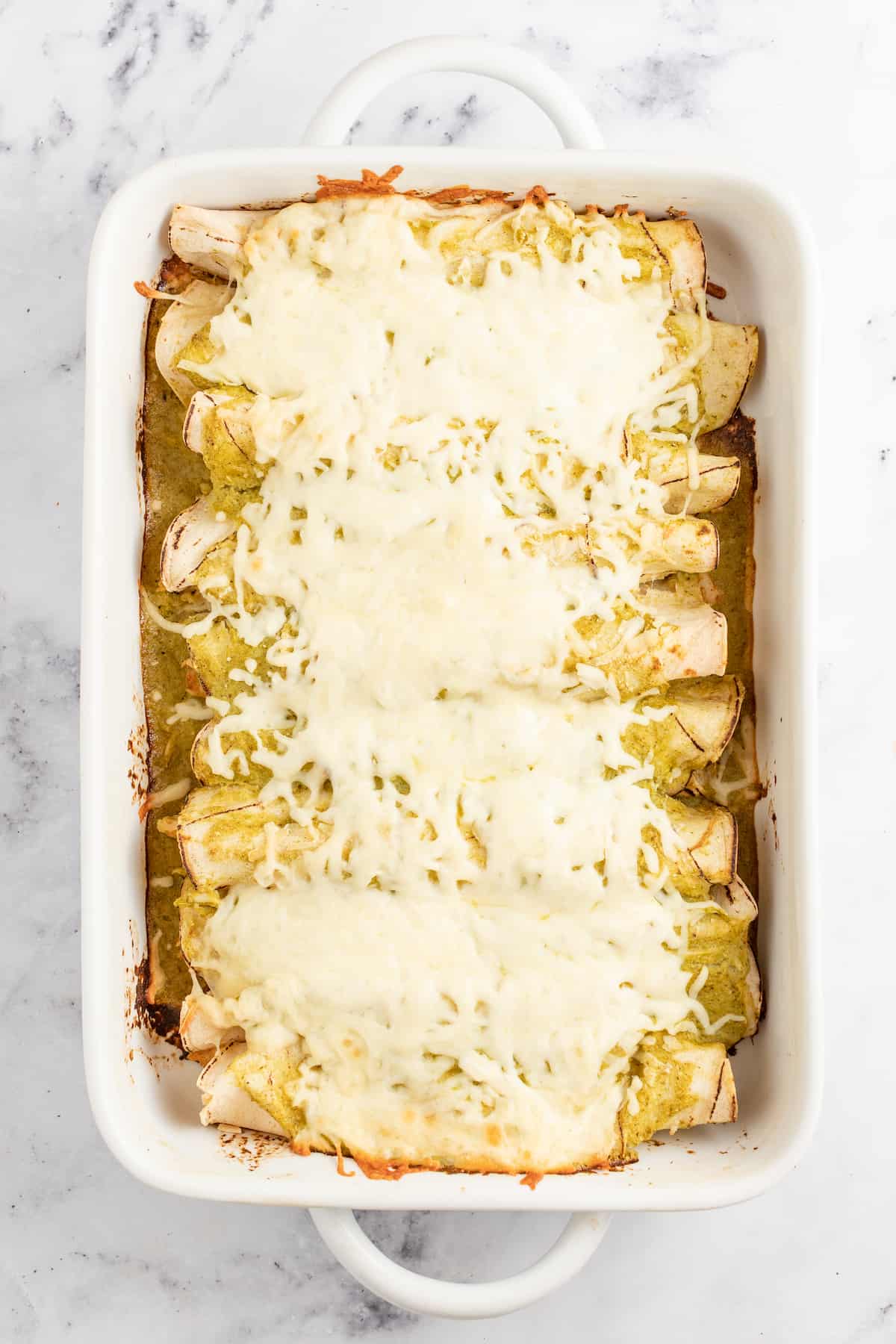 casserole dish with chicken enchiladas and cheese on top