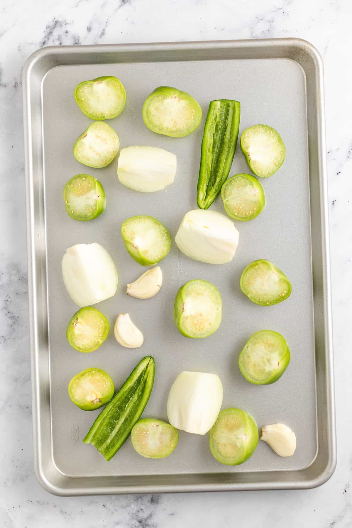 Creamy Chicken Enchiladas Verdes are perfect for big family dinners. They're cheesy and creamy with just the right amount of heat! raw ingredients on a sheet tray to make verde sauce like onions, tomatillos, and jalapenos