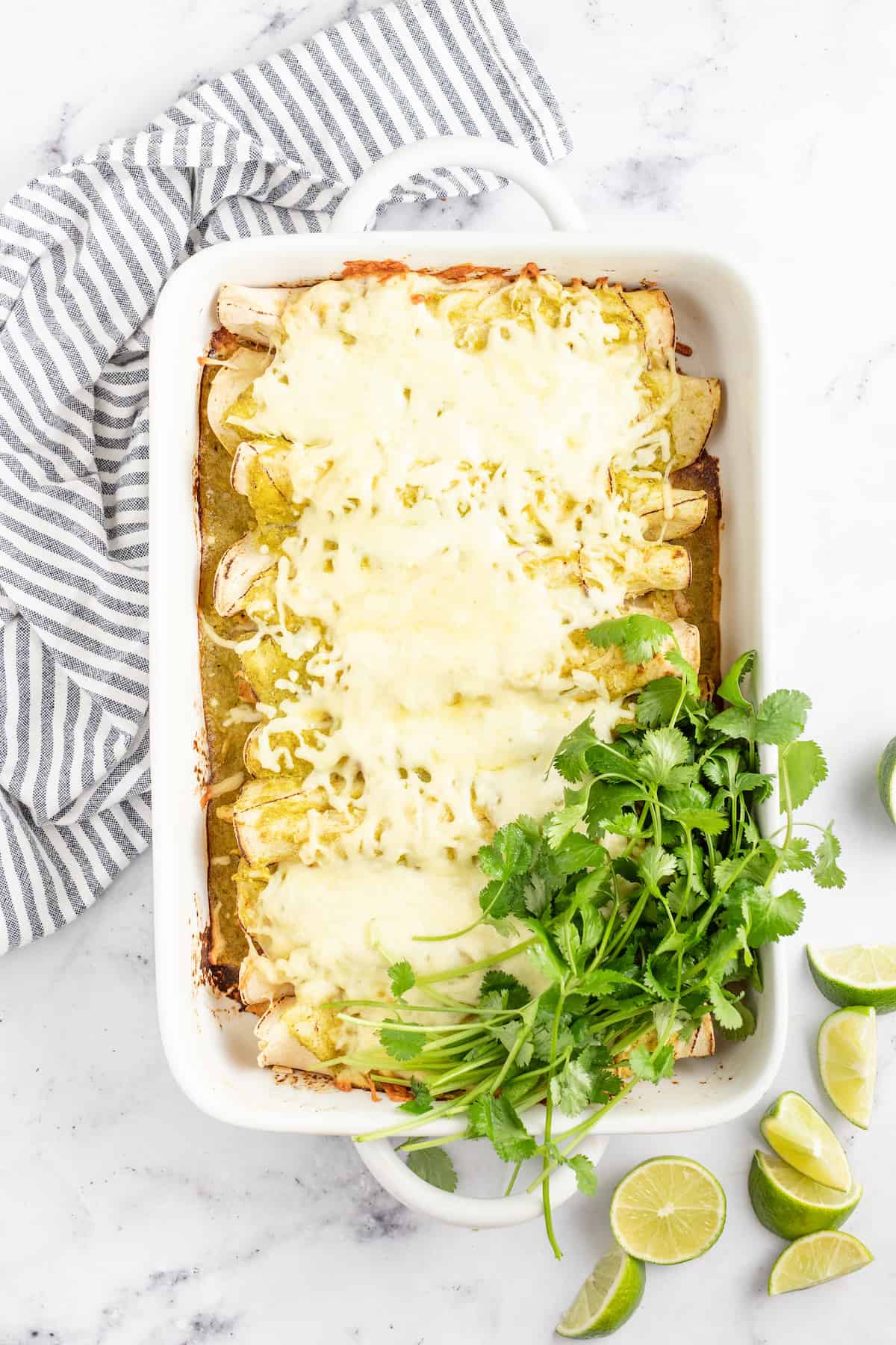 casserole dish with chicken enchiladas with melted cheese and cilantro on the side
