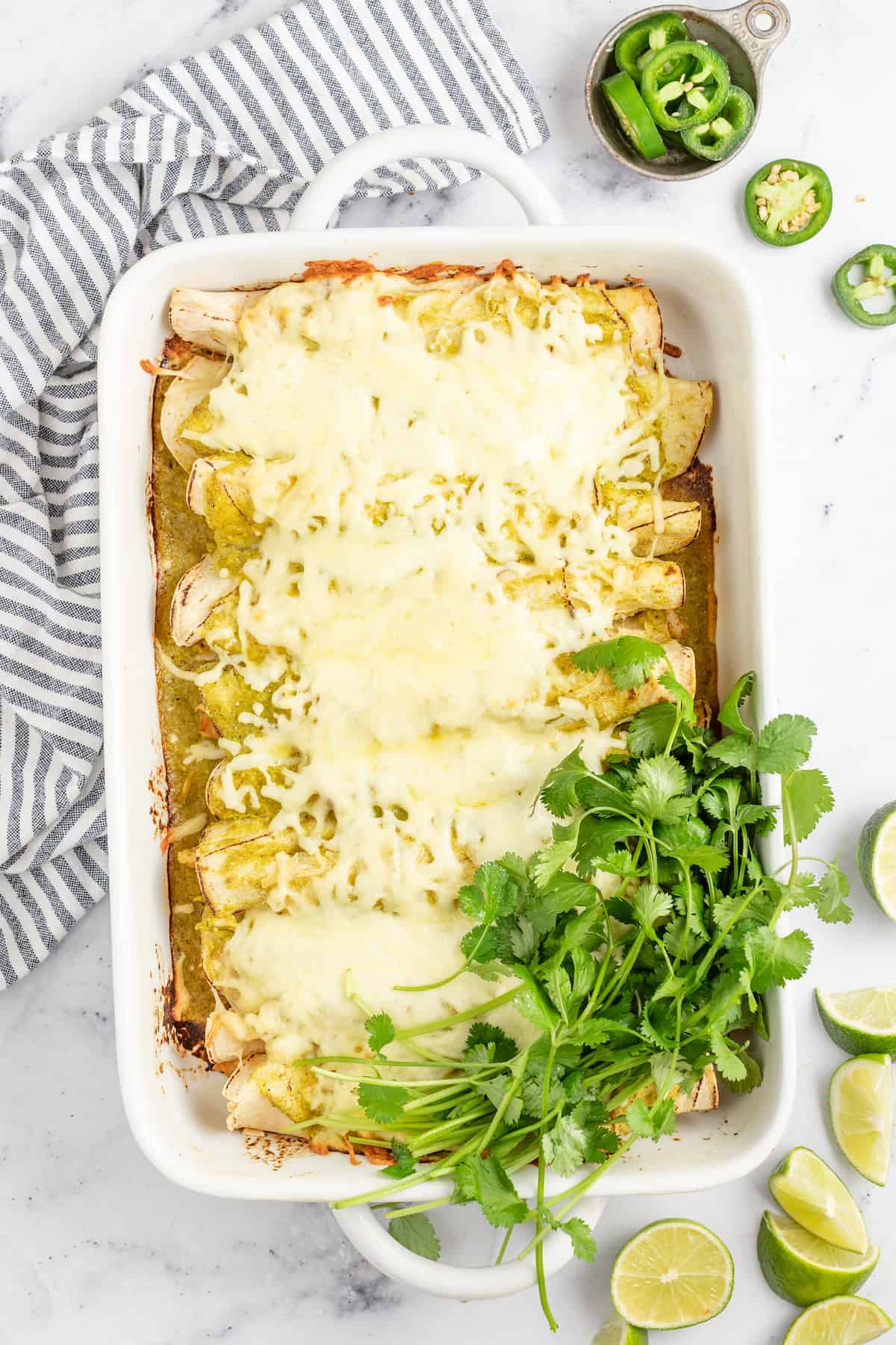 Creamy Chicken Enchiladas Verdes are perfect for big family dinners. They're cheesy and creamy with just the right amount of heat! casserole dish with chicken enchiladas with melted cheese and cilantro on the side