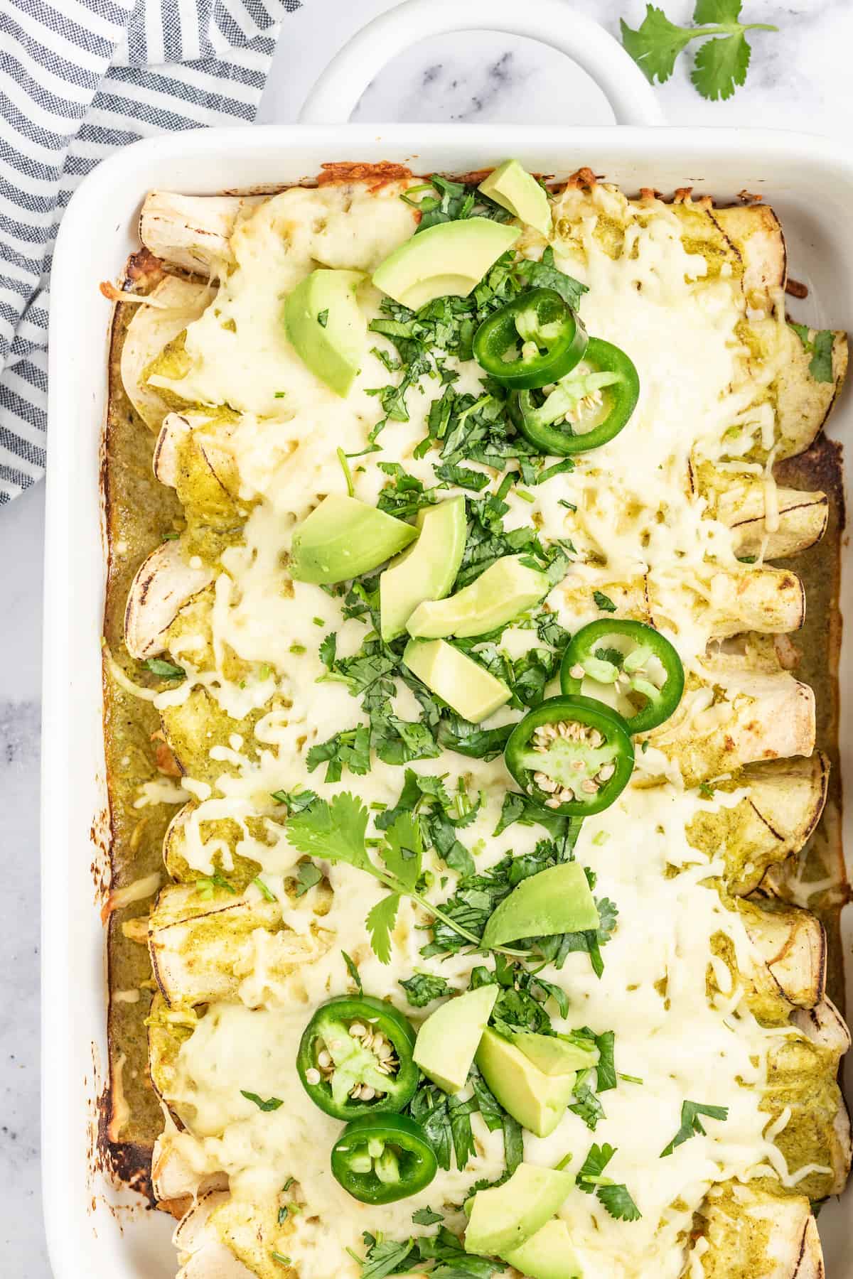 casserole dish with creamy chicken enchiladas verdes with limes and jalapenos as garnishes