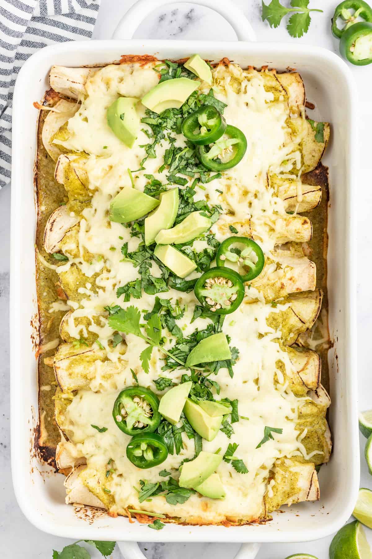 casserole dish with creamy chicken enchiladas verdes with limes and jalapenos as garnishes