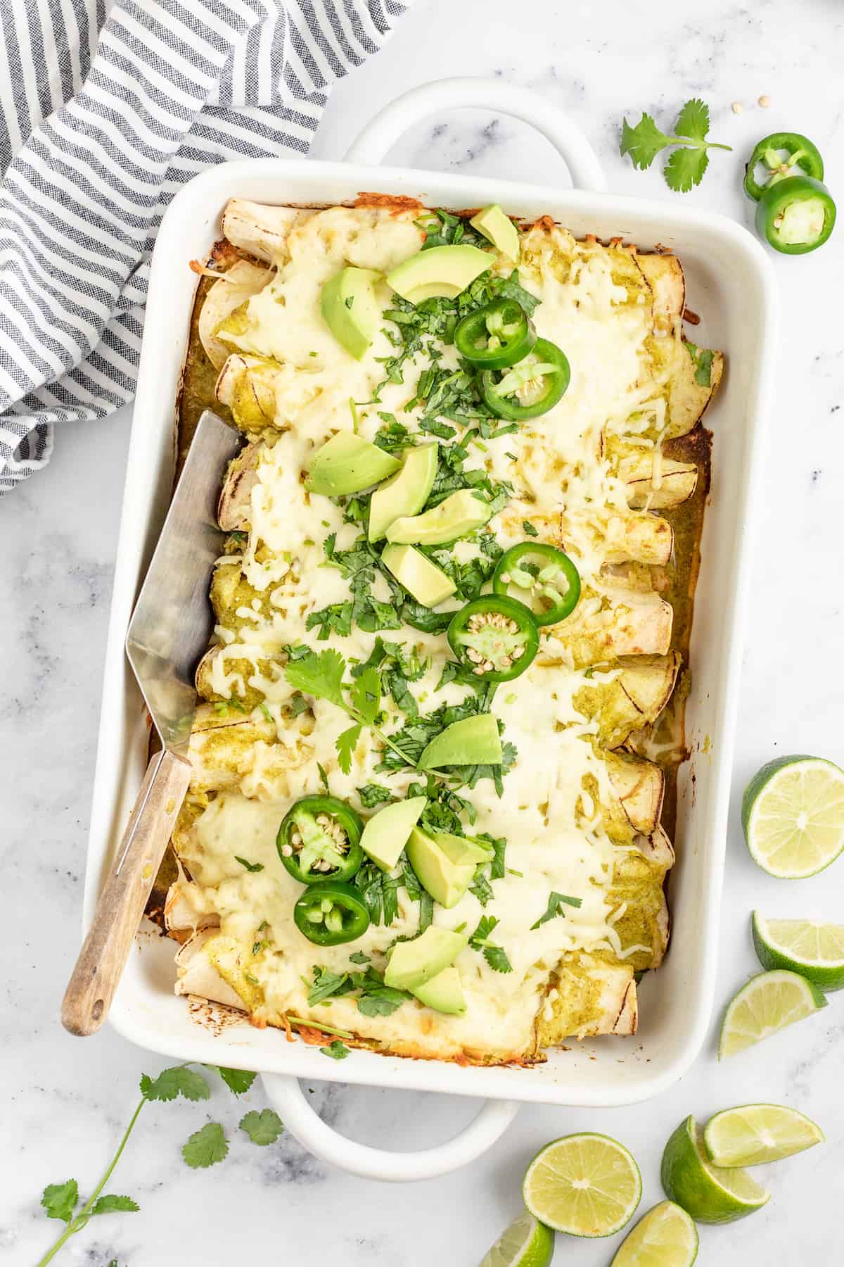 casserole dish with creamy chicken enchiladas verdes with limes and jalapenos as garnishes