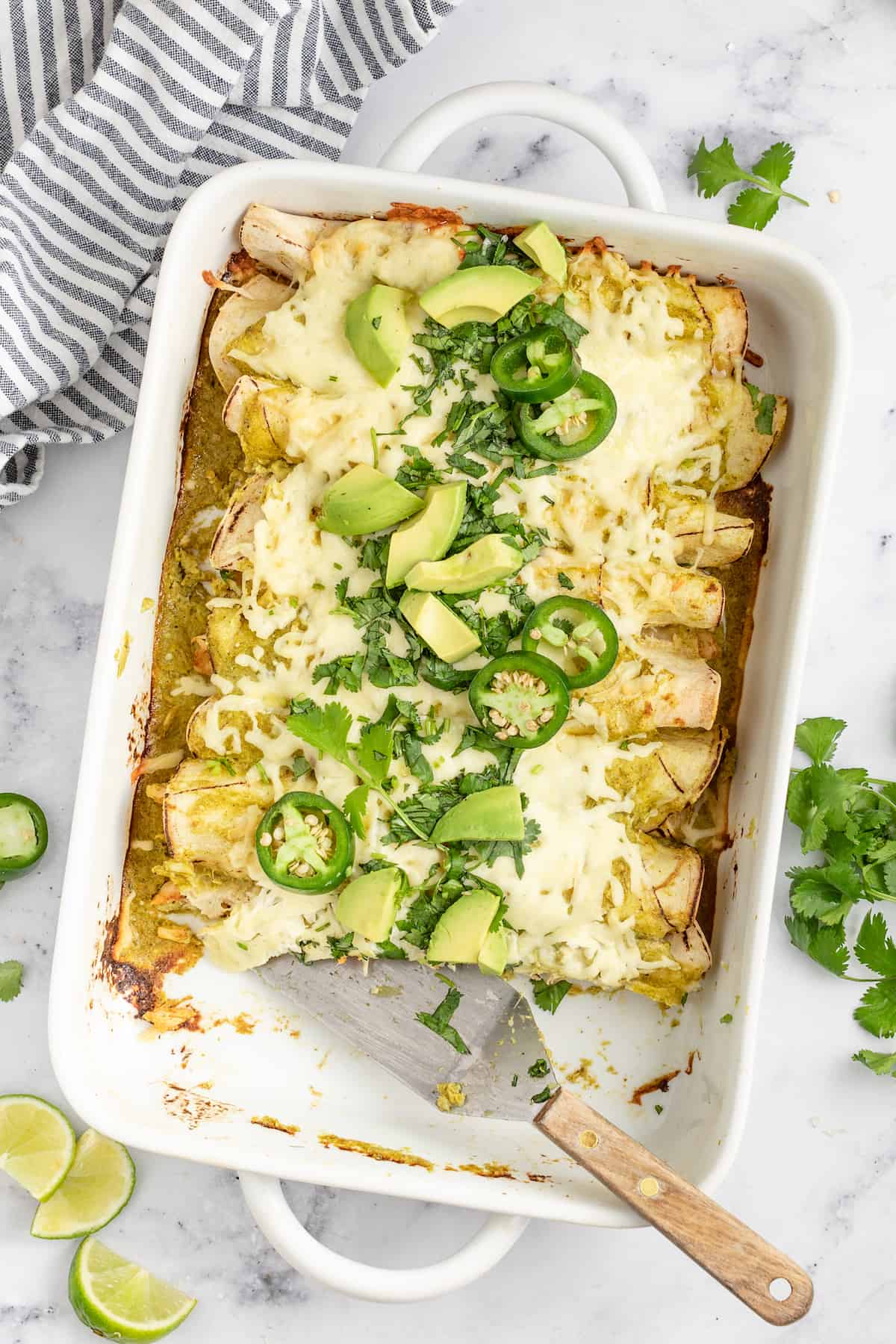 casserole dish with creamy chicken enchiladas verdes with limes and jalapenos as garnishes