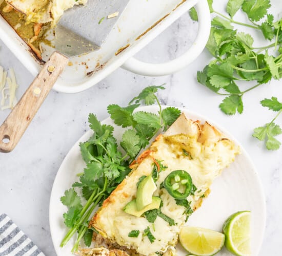 a plate with creamy chicken enchiladas verdes with lime and cilantro garnish