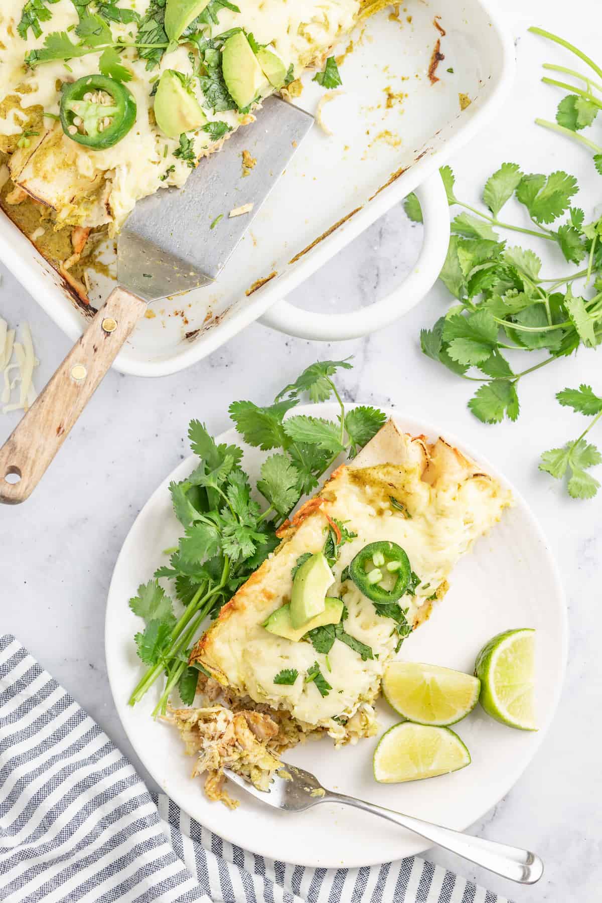 a plate with creamy chicken enchiladas verdes with lime and cilantro garnish