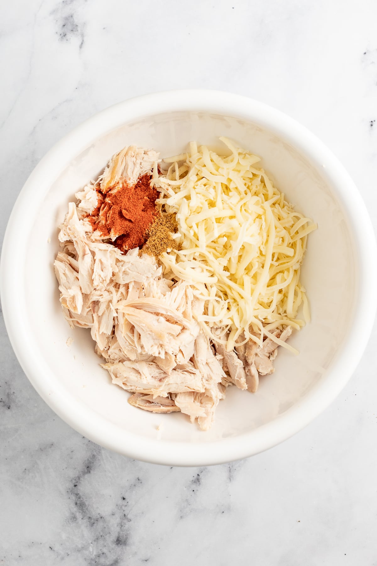 Creamy Chicken Enchiladas Verdes are perfect for big family dinners. They're cheesy and creamy with just the right amount of heat! a bowl with shredded chicken, cheese, and red seasoning