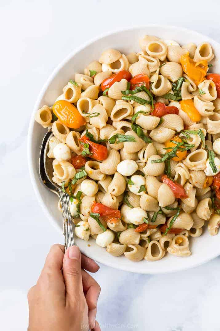 roasted tomato caprese pasta salad in a bowl with a hand holding a spoon