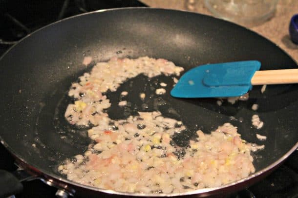 Shallots Sauteeing in a Pan with a Blue Rubber Spatula Stirring Them