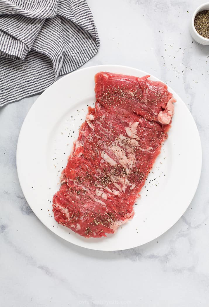 A raw skirt steak seasoned with salt and pepper on a white plate