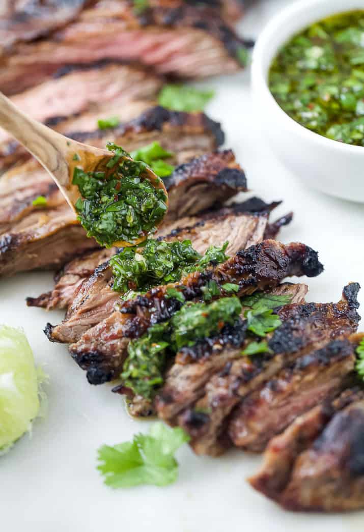 Chimichurri sauce being spooned on top of sliced skirt steak