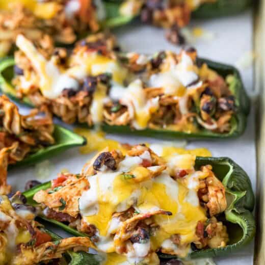 Close-up of stuffed poblano peppers with melty cheese on a baking sheet.