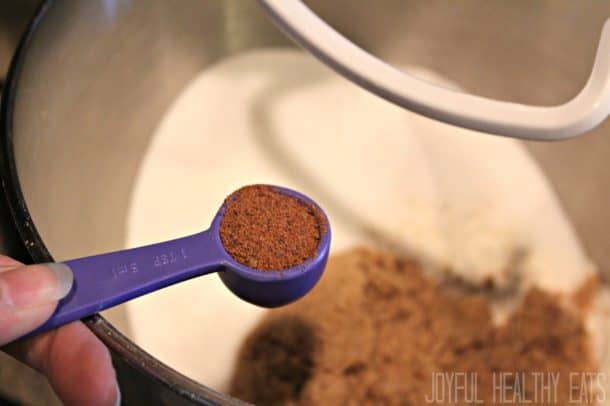 A teaspoon of cinnamon being added to a stand mixer bowl