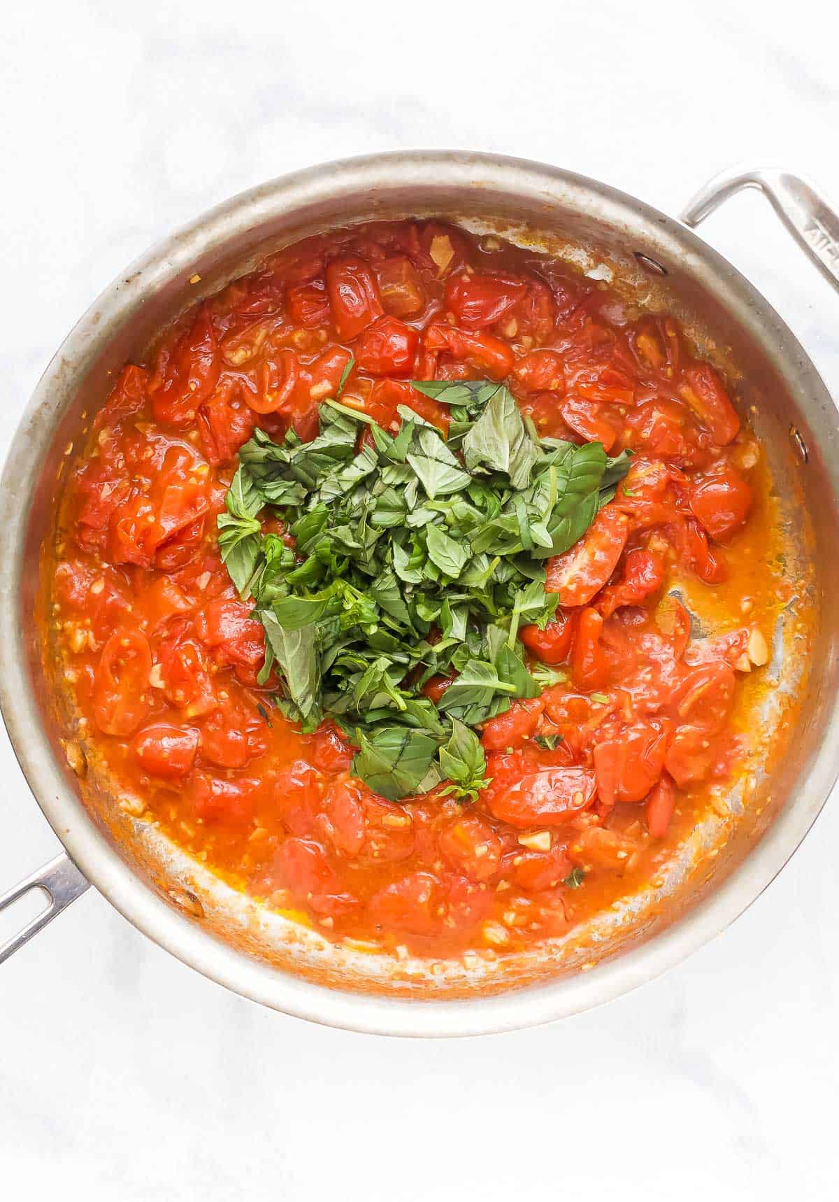 When you got this trusted pasta sauce recipe you will never buy a jar in the store again! Tomatoes, basil and lots of garlic make it delicious. The overhead view of the basil leaves has been added to the skillets of pasta sauce