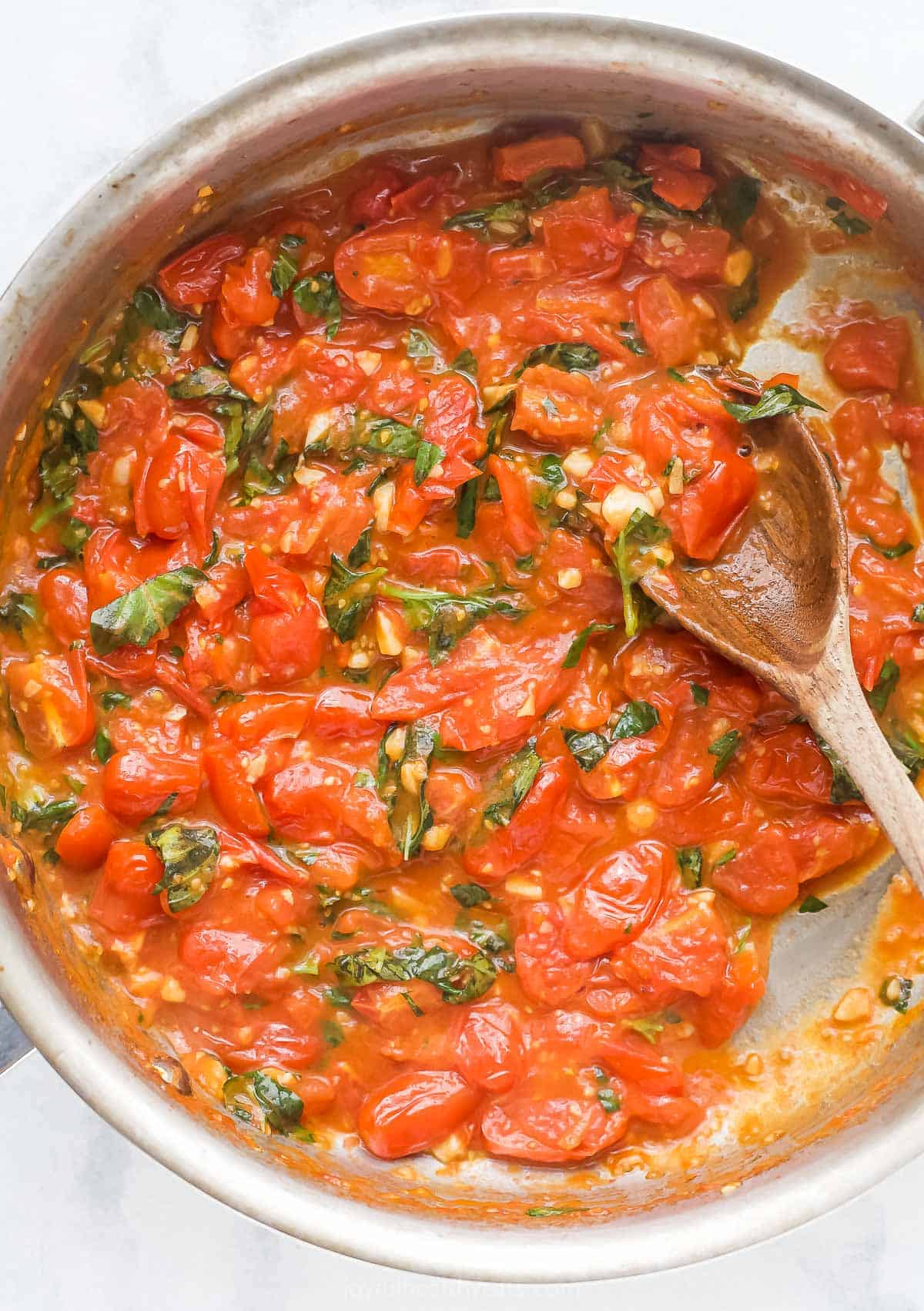 When you got this trusted pasta sauce recipe you will never buy a jar in the store again! Tomatoes, basil and lots of garlic make it delicious. Homemade pasta sauce overhead view in the skilllet with wooden spoon
