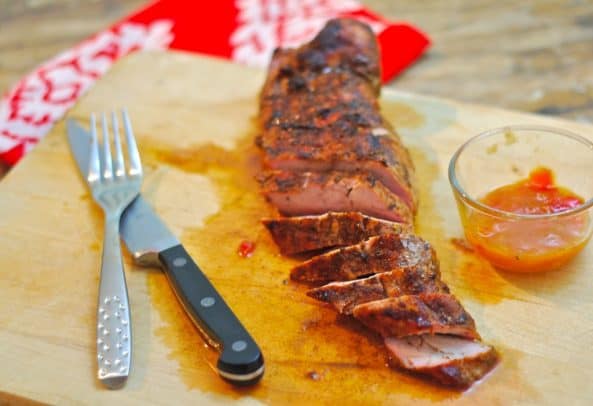 A Sliced Mango Chutney Pork Tenderloin on a Cutting Board with a Fork and Knife