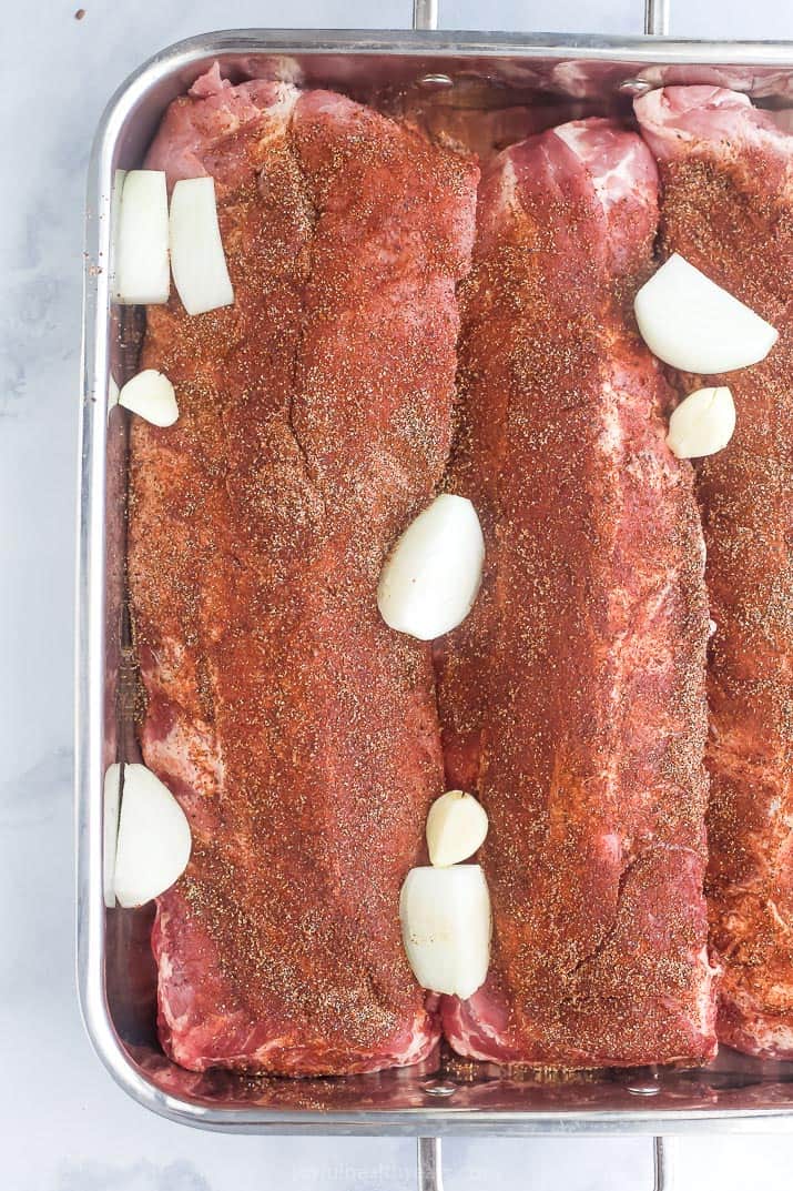 overhead photo of spice rubs baby back ribs in a dish with onions