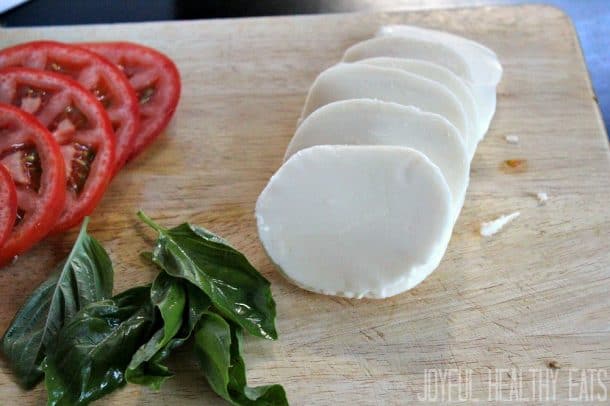 Sliced Tomato, basil, and fresh mozzarella on a cutting board