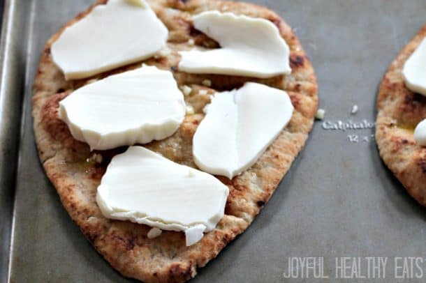 Flatbread topped with fresh sliced mozzarella on a baking sheet