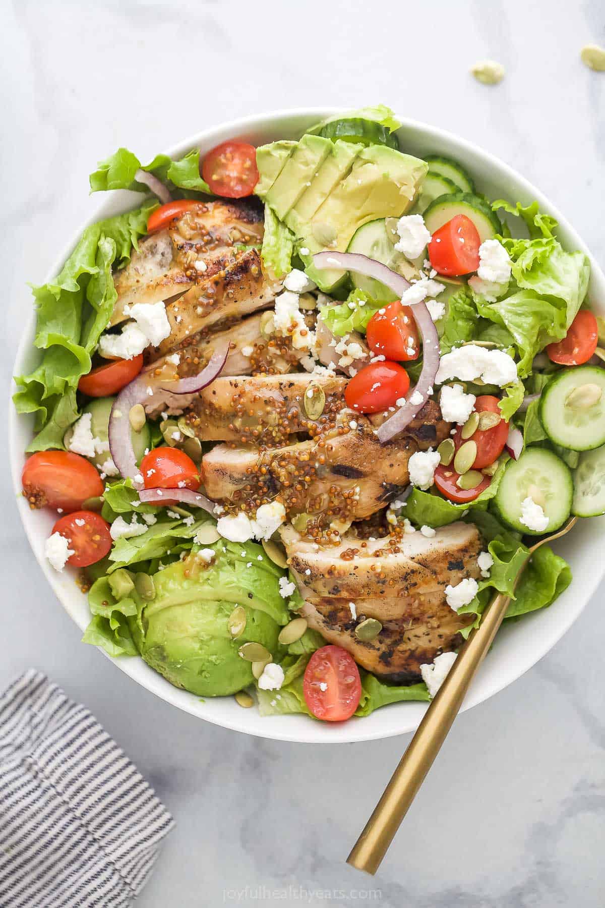 A bowl of chicken salad with avocado, cherry tomatoes and honey mustard dressing.