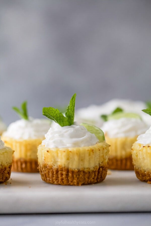 Mini key lime pies on marble board with whipped cream, mint, and lime for garnish