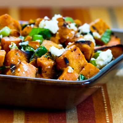 A square bowl of sweet potato salad with diced sweet potatoes, fresh herbs and crumbled cheese