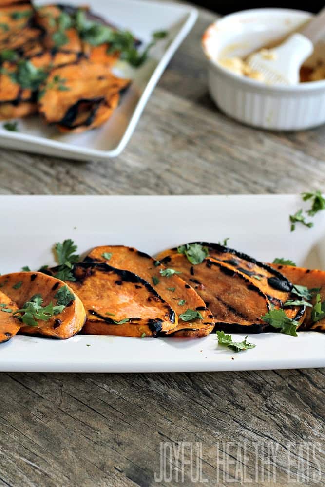 Grilled Sweet Potato slices on a platter with fresh herbs