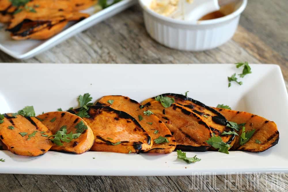 Grilled Sweet Potato slices on a platter with fresh herbs
