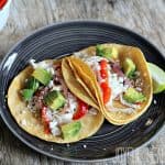 Two shredded Chicken Tacos on a black plate with a lime