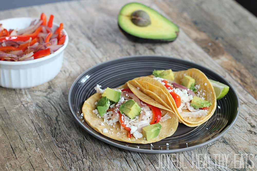 Two Chicken Tacos on a plate that is sitting on a wood table with taco ingredients 