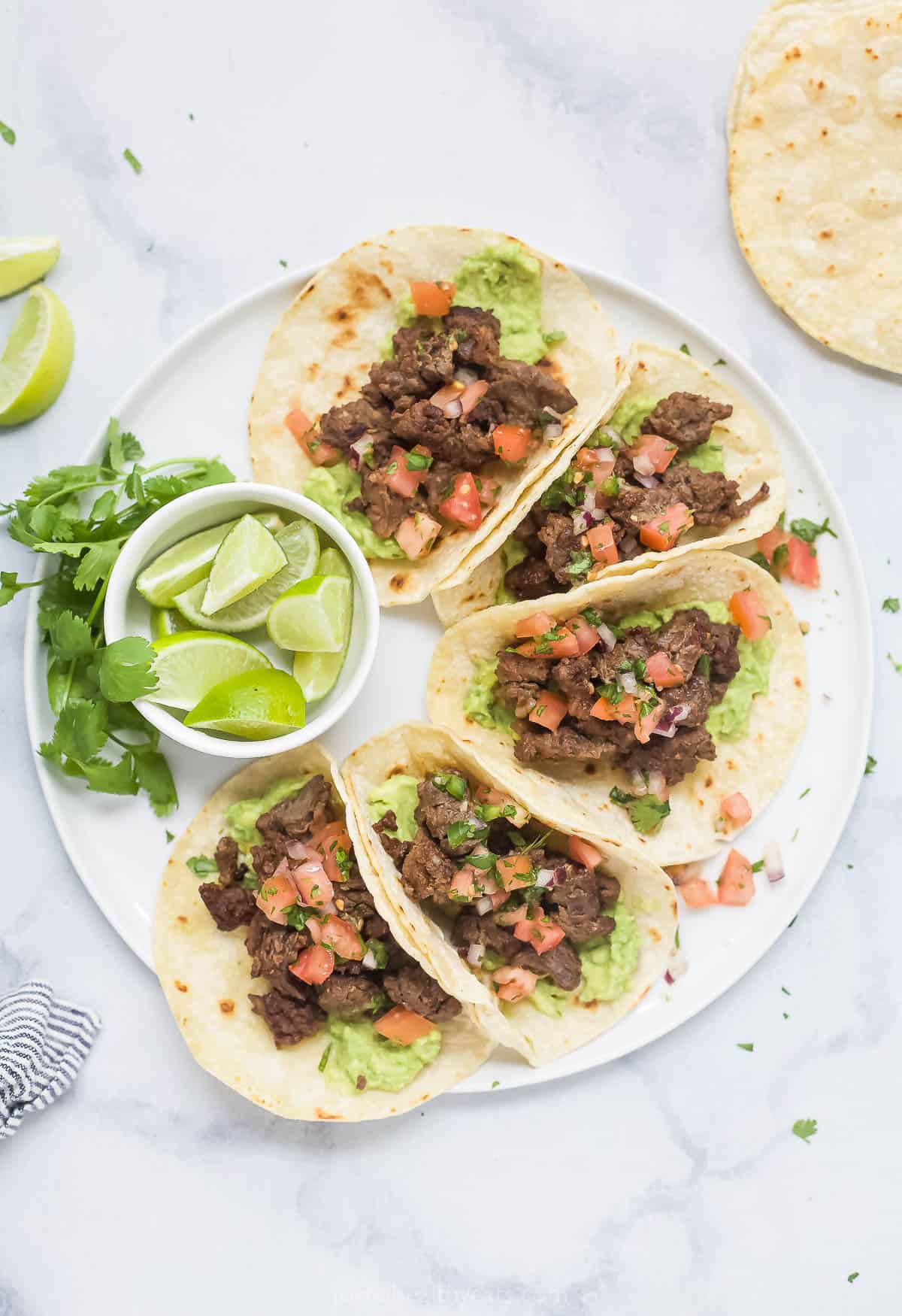 Plate of skirt steak tacos with a bowl of lime wedges on the side. 