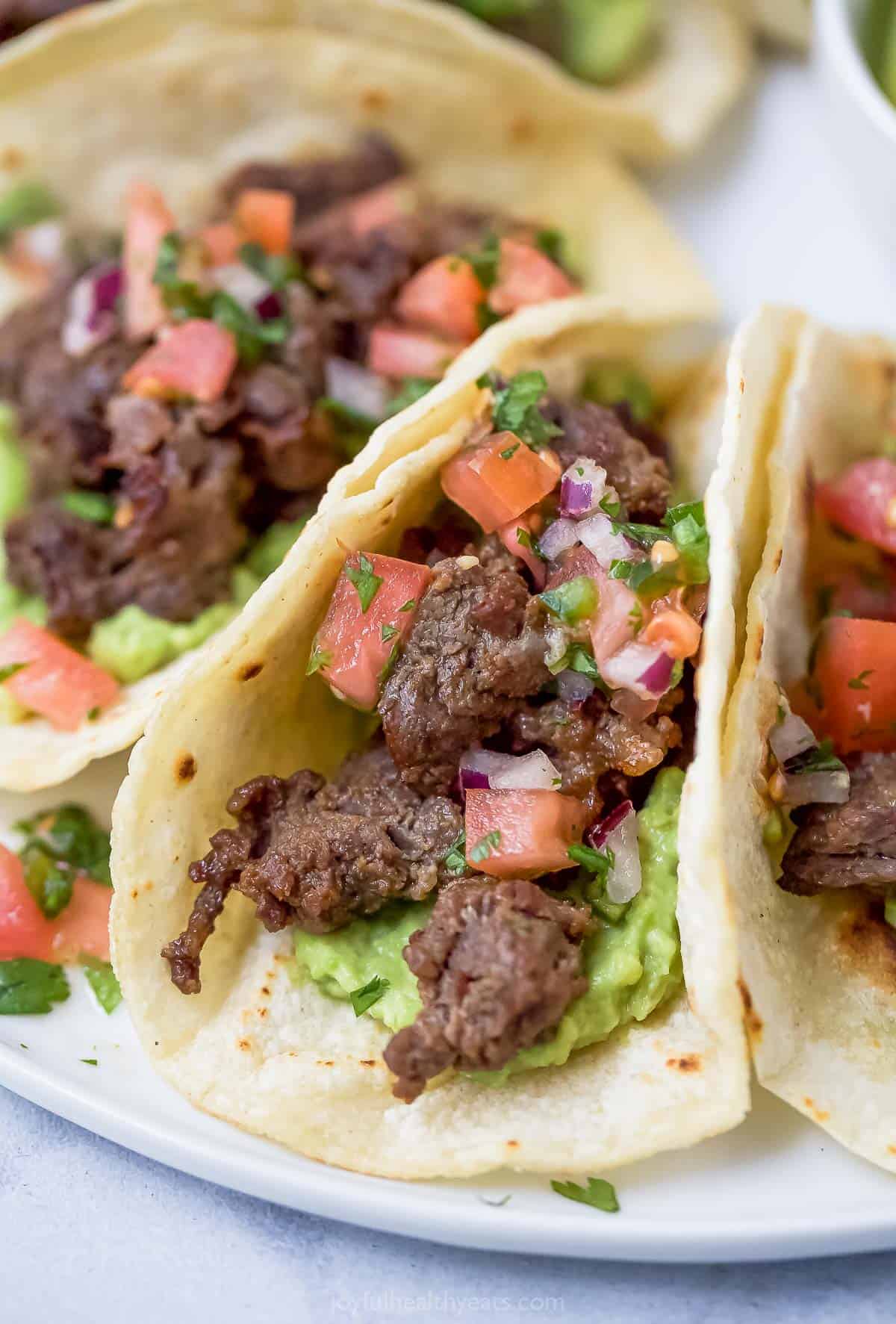 Close-up of skirt steak tacos with diced tomatoes, onions, and guacamole. 